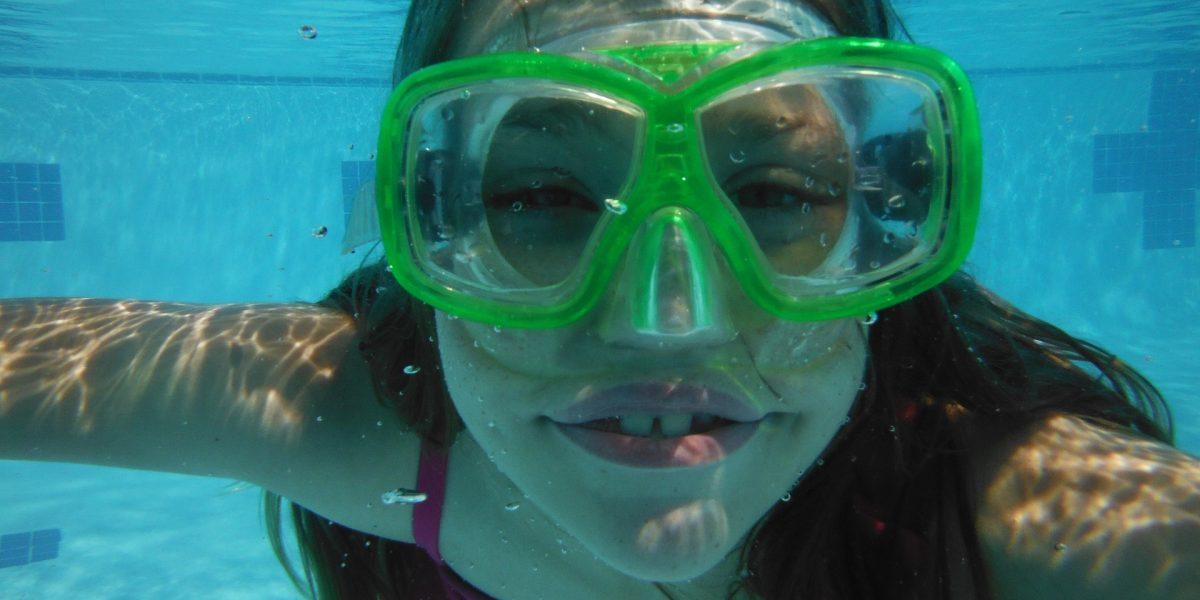 Chica buceando en una piscina con sus gafas de bucear mientras está sonriendo