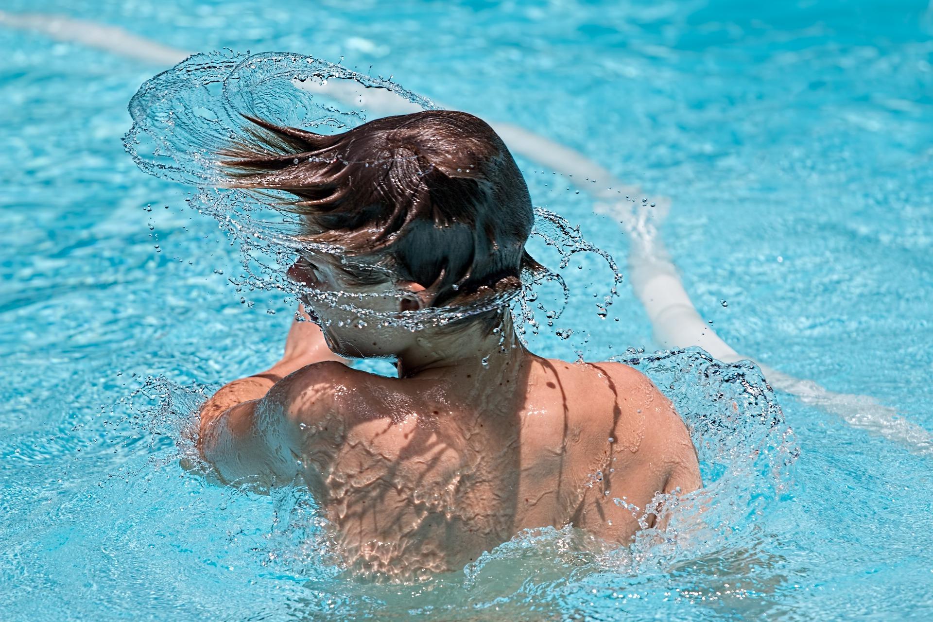 Chico secándose el pelo en una piscina donde se pueden apreciar las gotas de agua salpicándose entre ellas