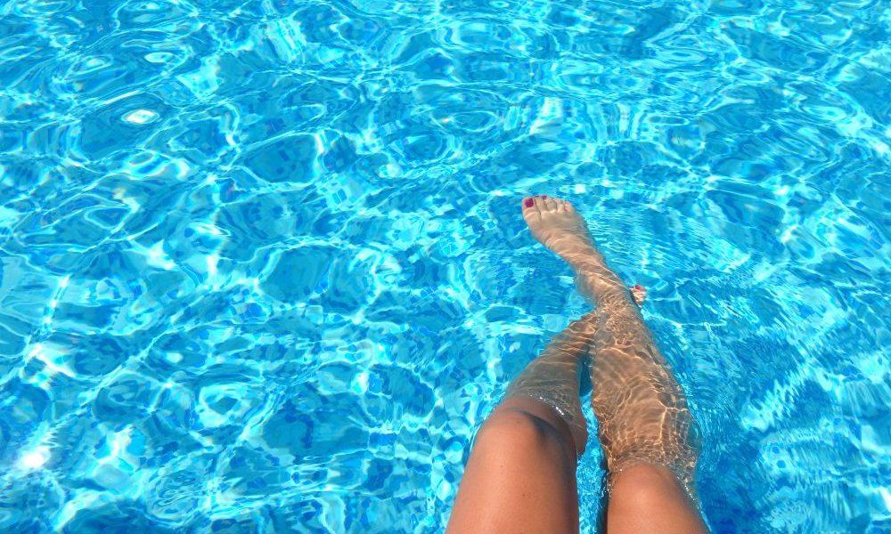 Chica mojándose los pies en la piscina mientras disfruta de un día soleado